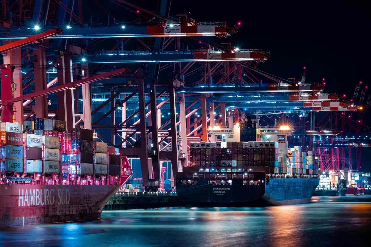 Port commercial la nuit avec navire chargé de conteneurs et grues de manutention illuminées
