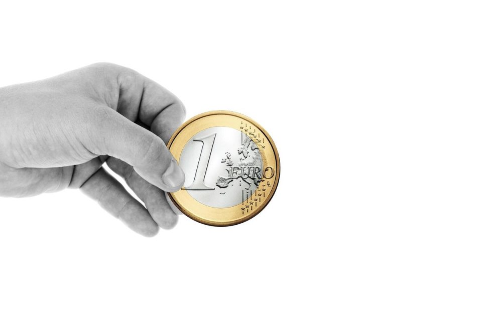 Main tenant une pièce de 1 euro avec face et revers visibles sur fond blanc