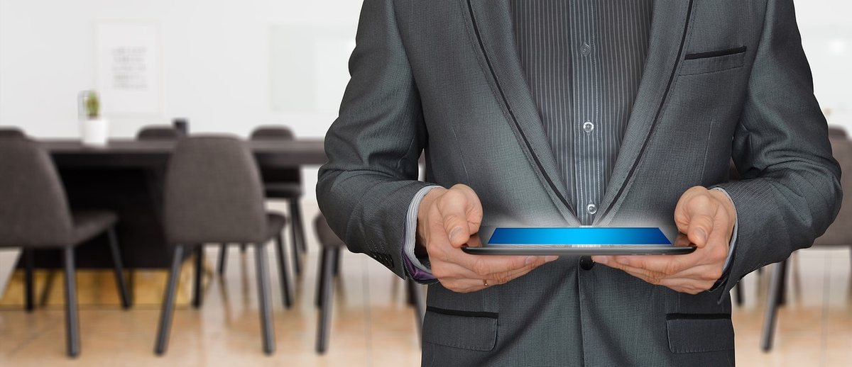 Homme en costume noir tenant une tablette lumineuse dans une salle de réunion