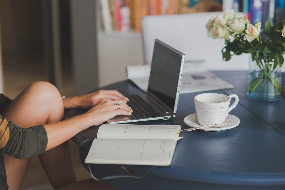 Femme travaillant sur ordinateur portable avec livre et tasse de café à côté