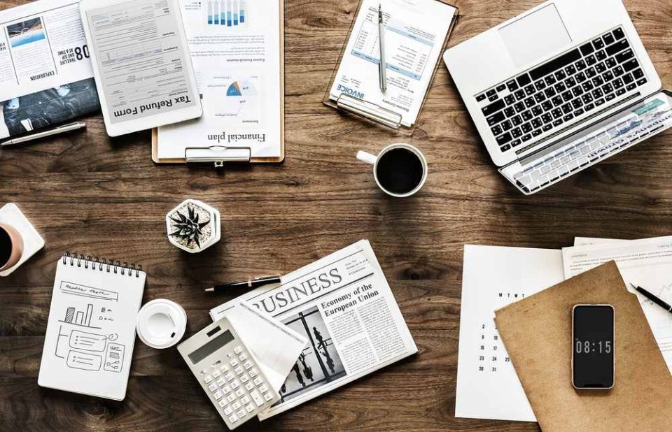 Ordinateur, documents, téléphone, café, agenda, calculatrice, feuilles sur un bureau en bois