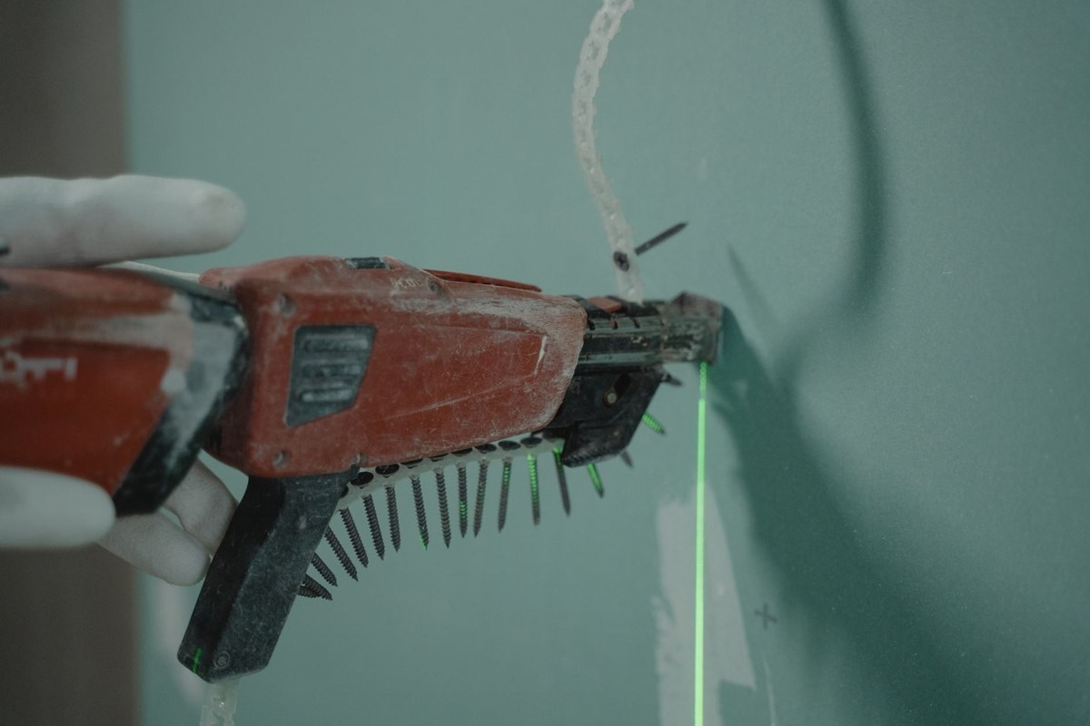 Une main gantée tient une perceuse à clous sur un mur avec laser vert